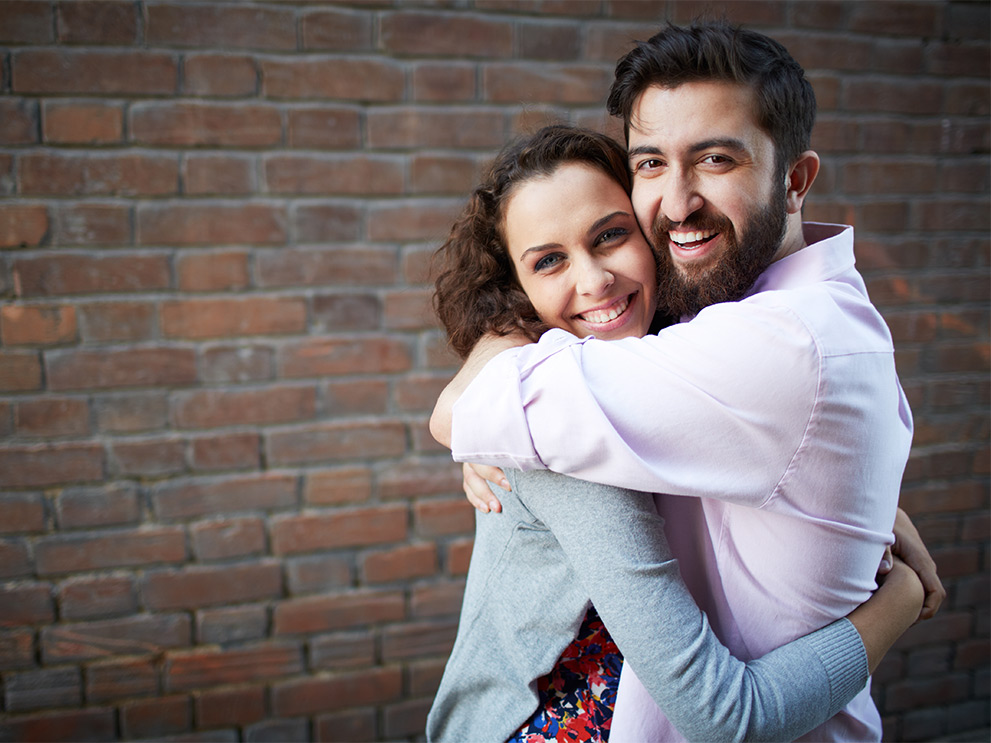 Couple hugging next to a brick wall